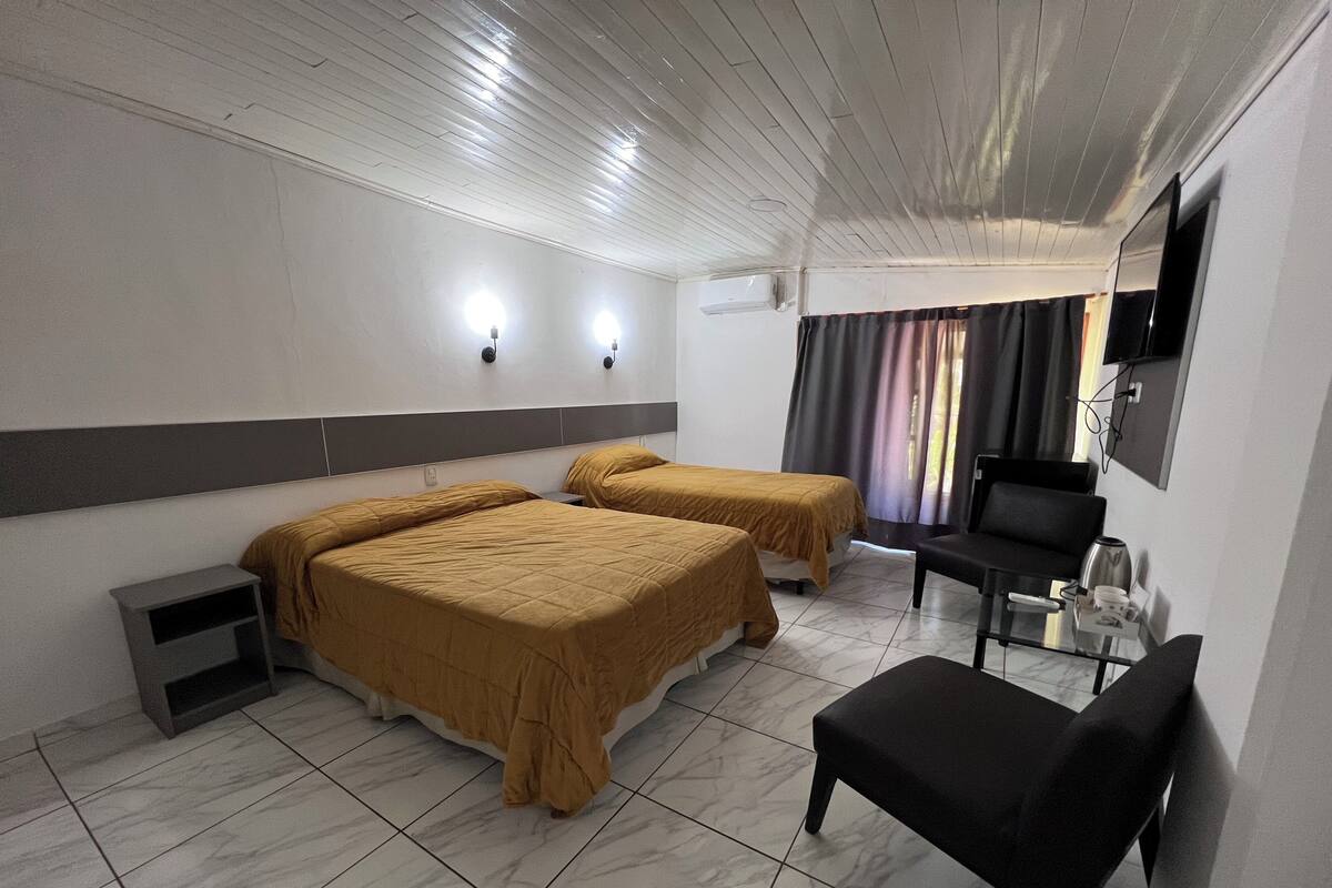 A hotel room with two beds, a small table, a chair, a TV, and a window with curtains.