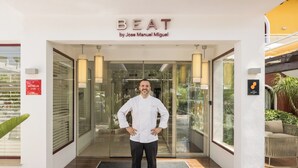 Uno chef in piedi davanti all'ingresso di un ristorante chiamato 'BEAT by Jose Manuel Miguel', con una vetrata, un cartello che indica Michelin 2026 e vista dell'esterno.