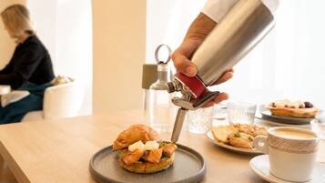 A person pouring a drink into a cup on a table with food items and a bottle in the background.