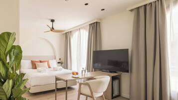 Moderni hotellihuone, jossa on sänky, televisio, ruokapöytä ja kattotuuletin.