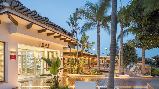 Un hotel con il cartello 'BEAT', posti a sedere all'aperto, palme e un ingresso ben illuminato.