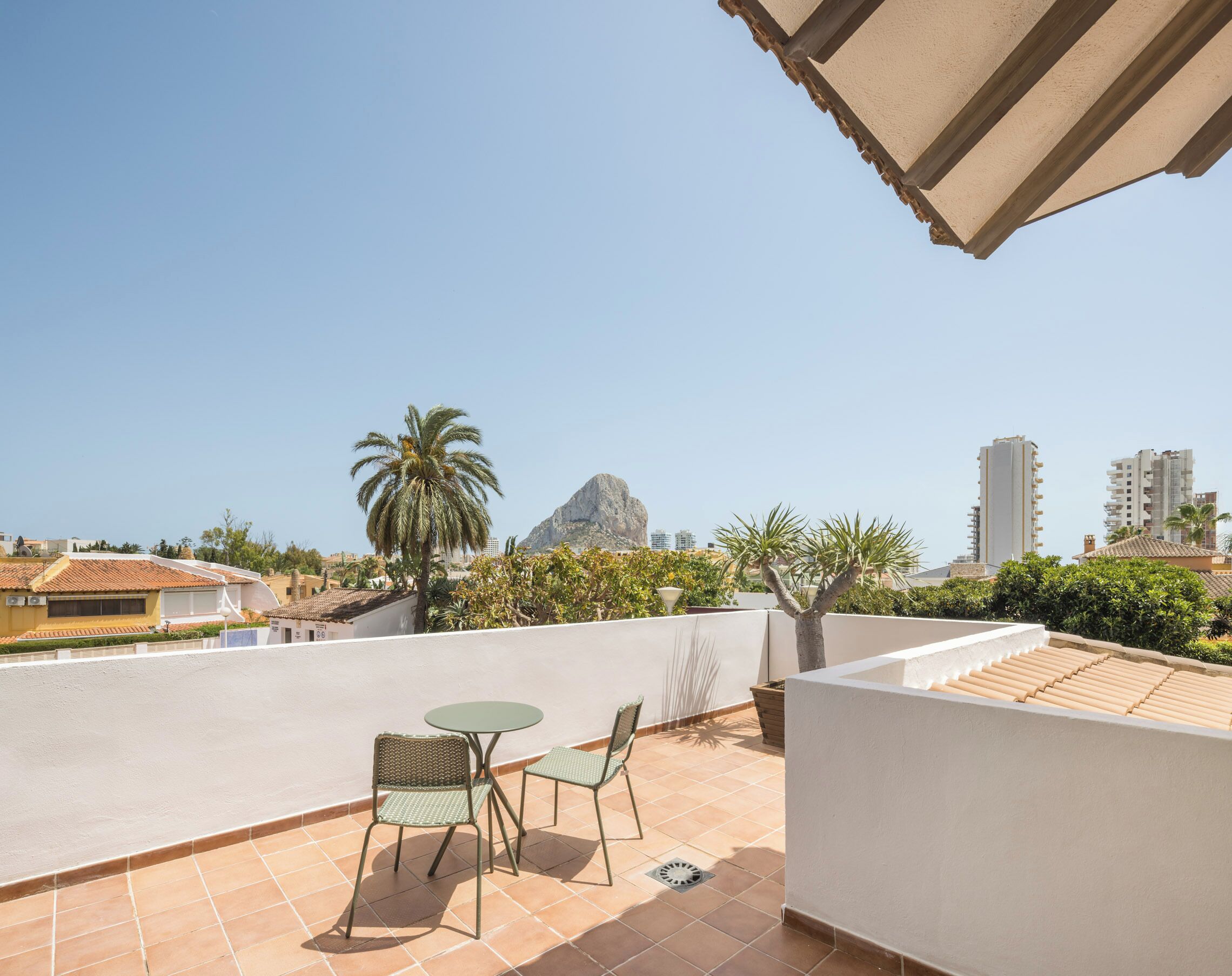 Una terraza en la azotea con una mesa y sillas, una palmera y una montaña al fondo.