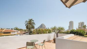 Una terraza en la azotea con una mesa y sillas, una palmera y una montaña al fondo.
