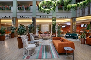Un hall amplio con varias zonas de estar, incluyendo sofás y sillones, rodeado de grandes macetas con plantas y un mostrador de recepción central.