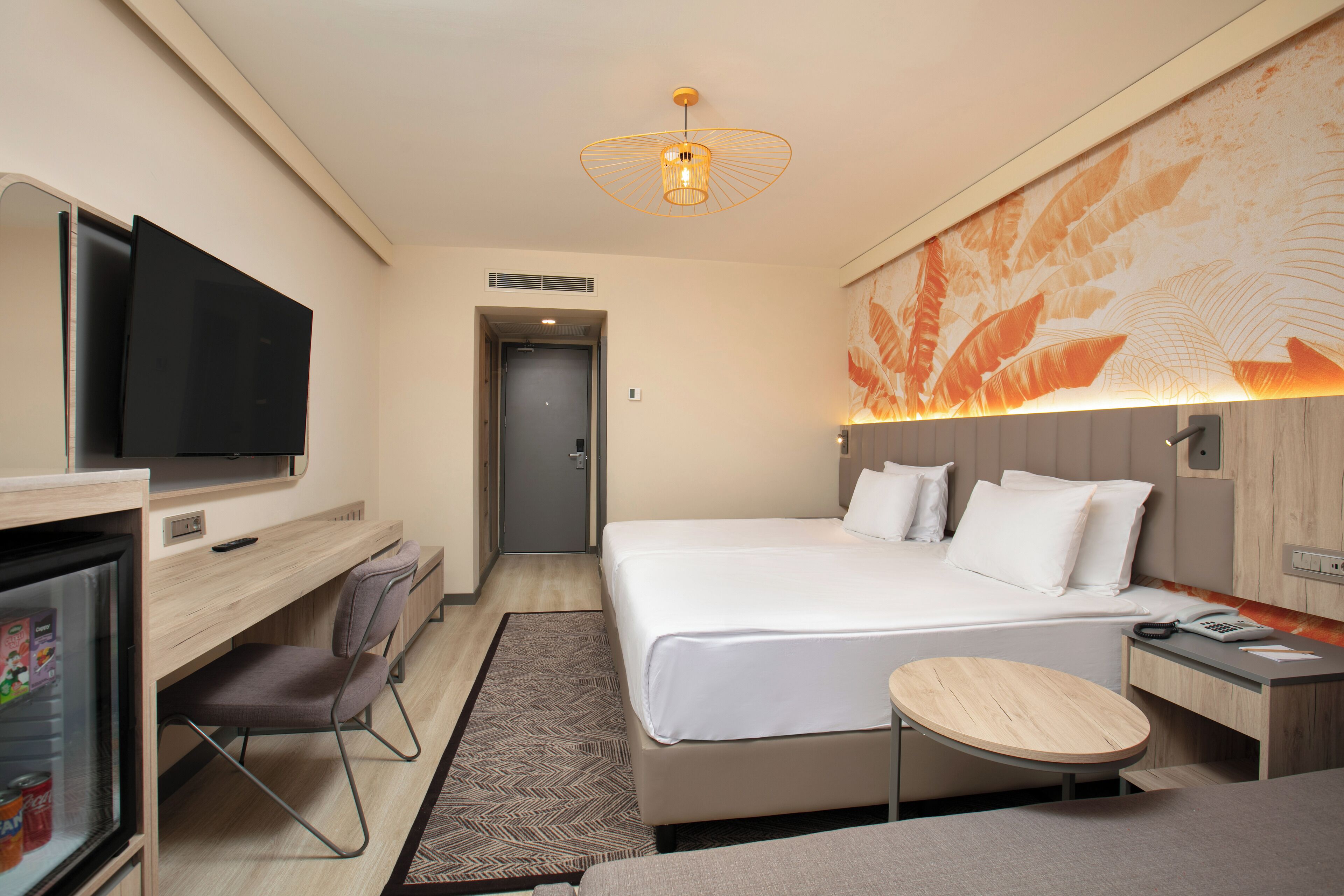Hotelkamer met een bed, een bureau met een televisie, een stoel, een klein tafeltje en een muur met een bladpatroon.
