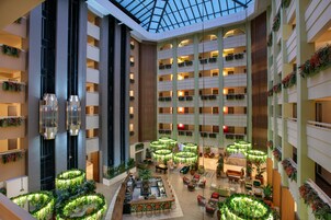 Un vestíbulo de hotel de varios niveles con techo de cristal, múltiples balcones y jardines interiores.
