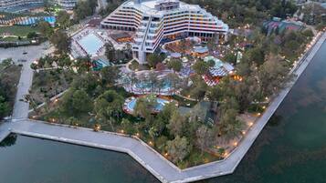 Et stort hotel med flere etager, en swimmingpool og et anlagt område med træer og en bro.