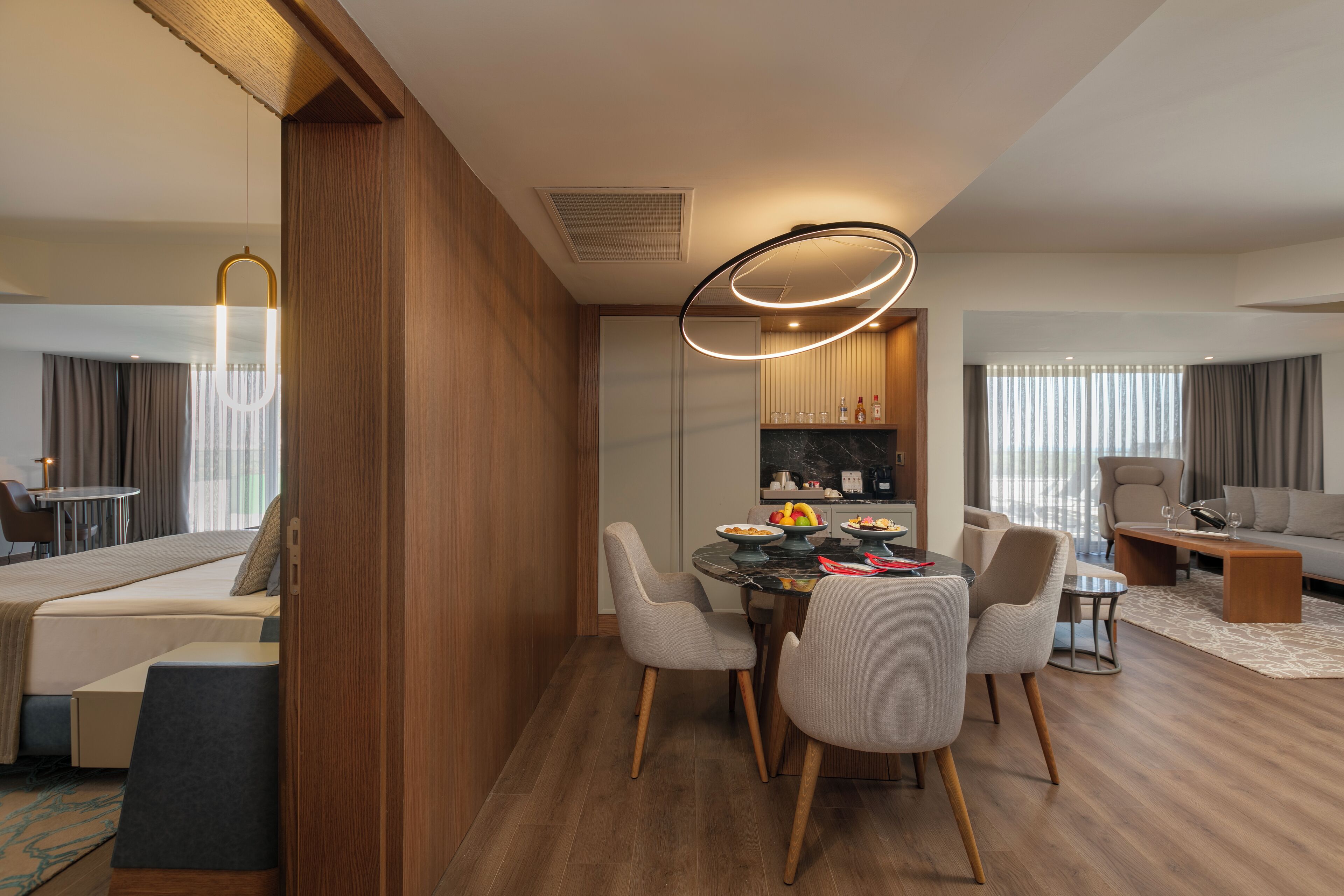 A modern hotel room with a dining area, a sofa, and a kitchen.