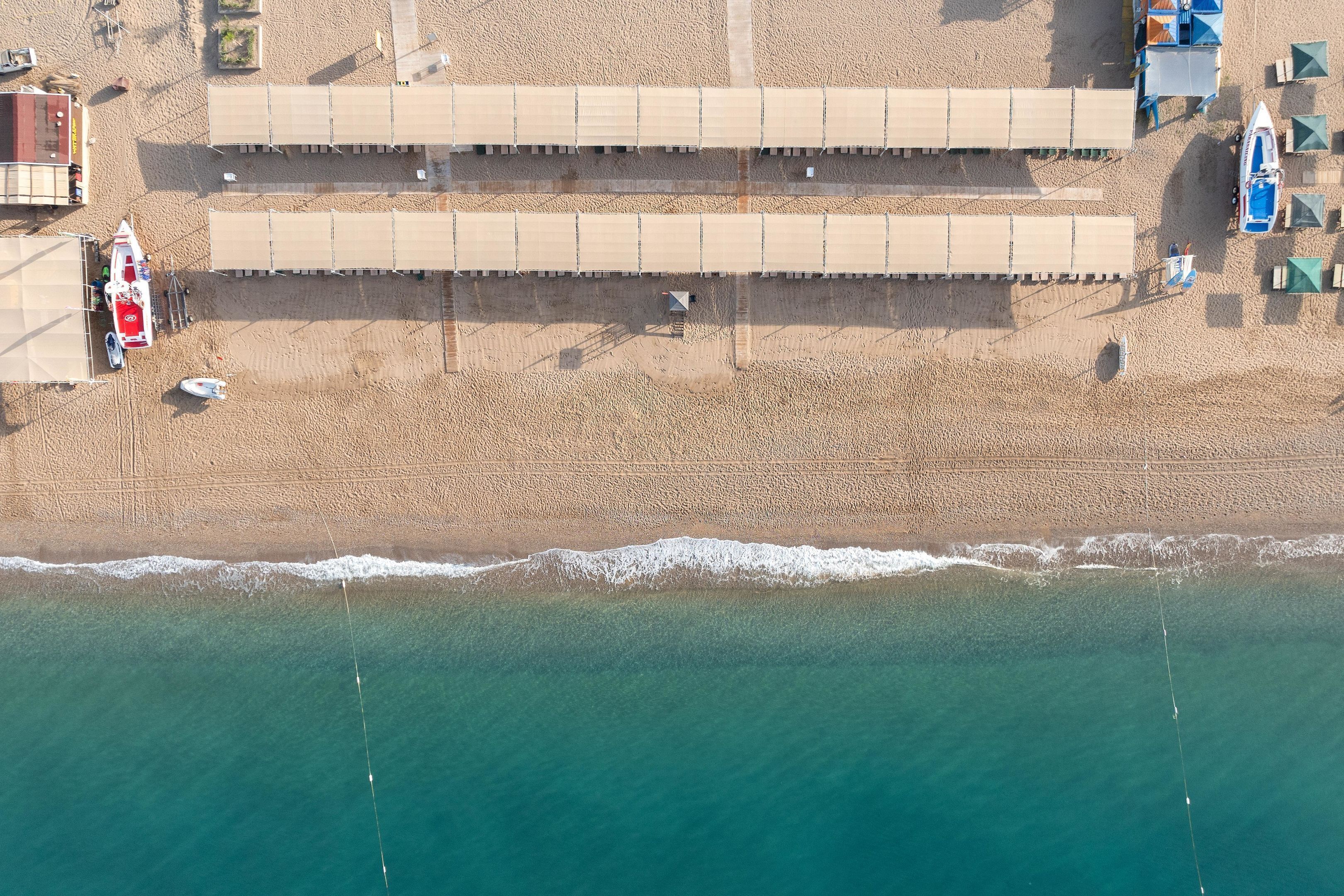 Vista aérea de una playa con una hilera de cabañas de playa, una torre de salvavidas y una lancha pequeña.