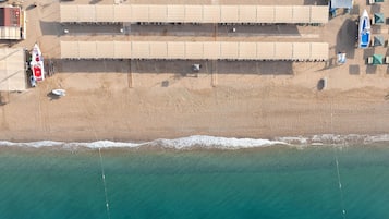Vista aérea de una playa con una hilera de cabañas de playa, una torre de salvavidas y una lancha pequeña.