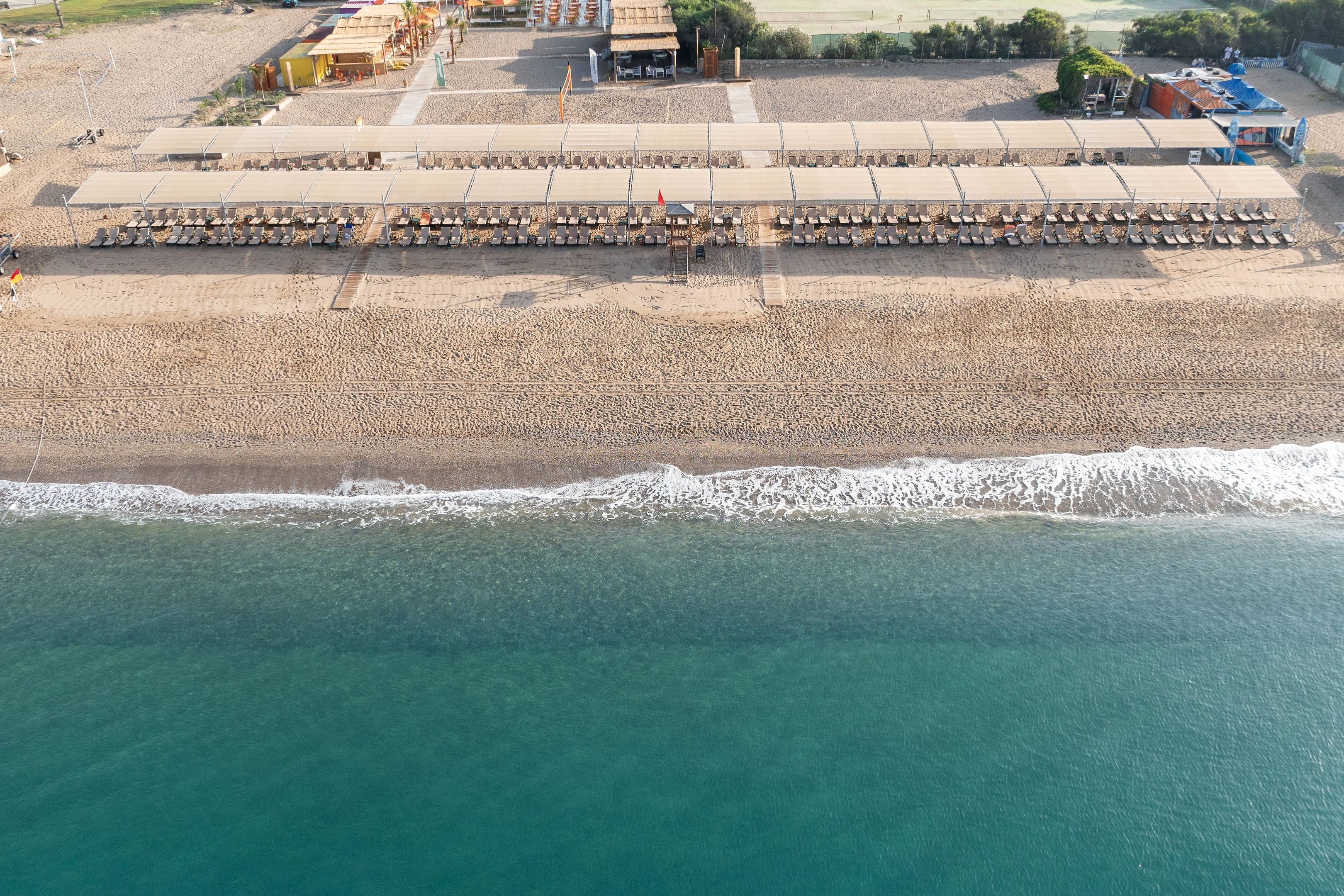 Vista aérea de una playa con una larga fila de sillas y sombrillas, arena dorada y un océano azul cristalino.