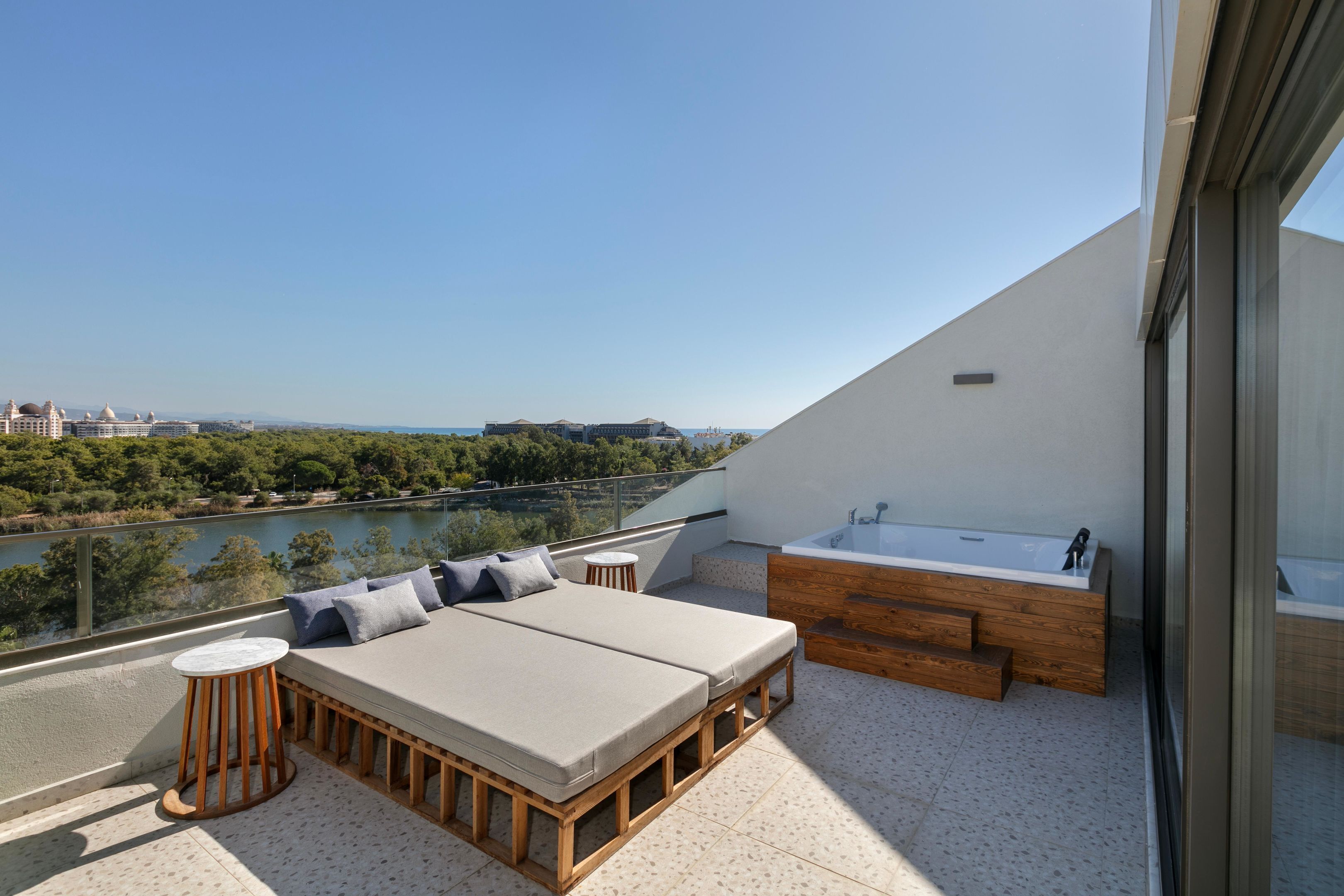 Un balcón con vista al río, una banca de madera, una mesita y una bañera.