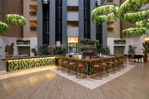 A modern bar area with a wooden counter, multiple stools, and hanging greenery. - Megasaray Resort Side (Manavgat)