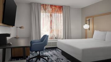 A hotel room with a bed, desk, chair, TV, and a window with curtains.