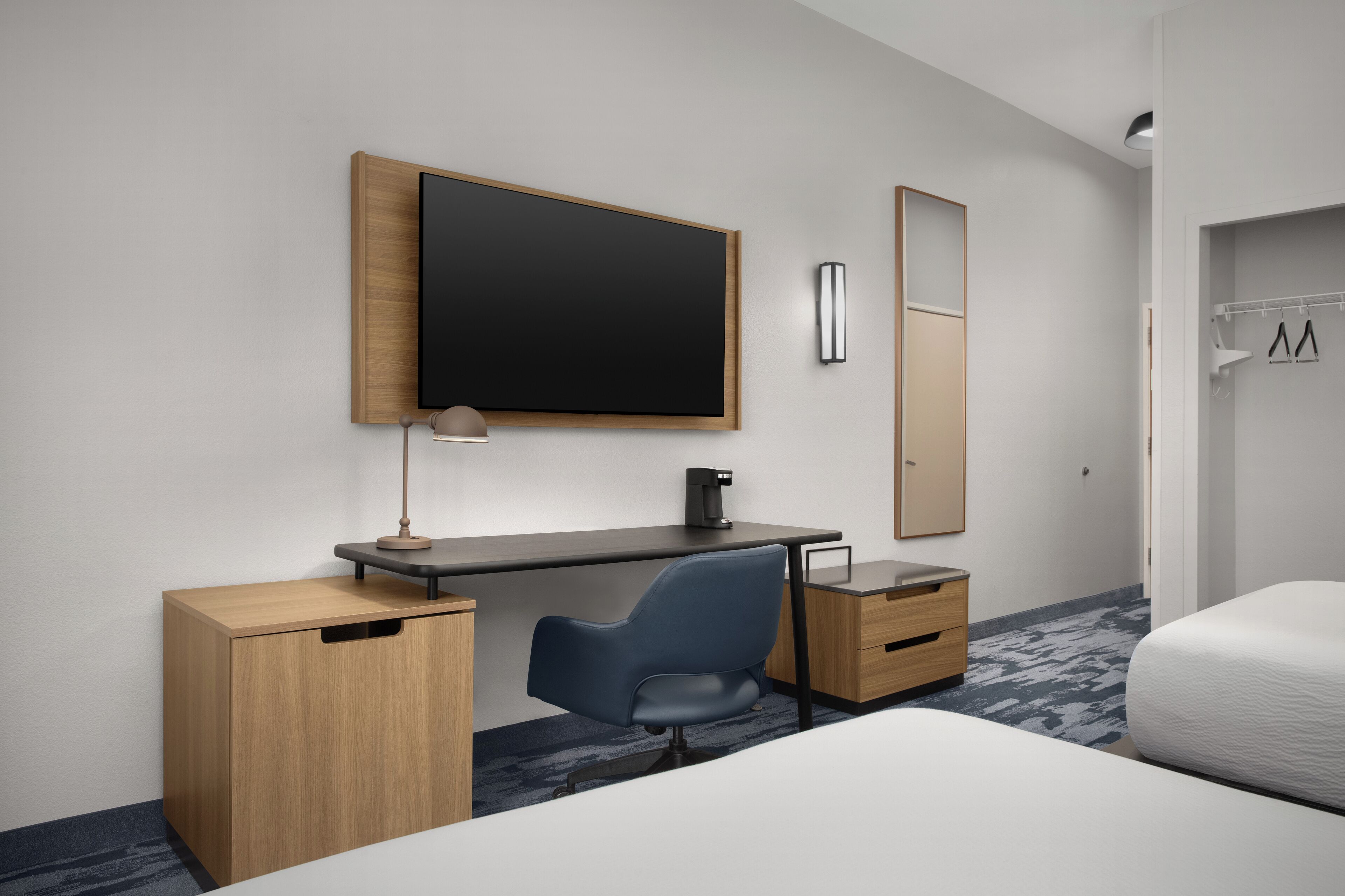 Una habitación de hotel moderna con un escritorio de madera, una silla negra, un televisor de pantalla plana, una mesita de noche y una cama.
