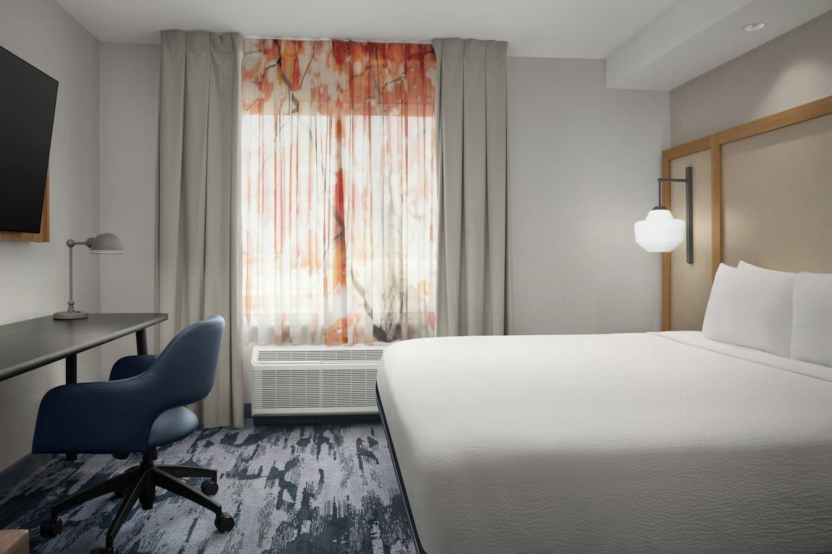 A hotel room with a bed, desk, chair, and a large window with curtains.