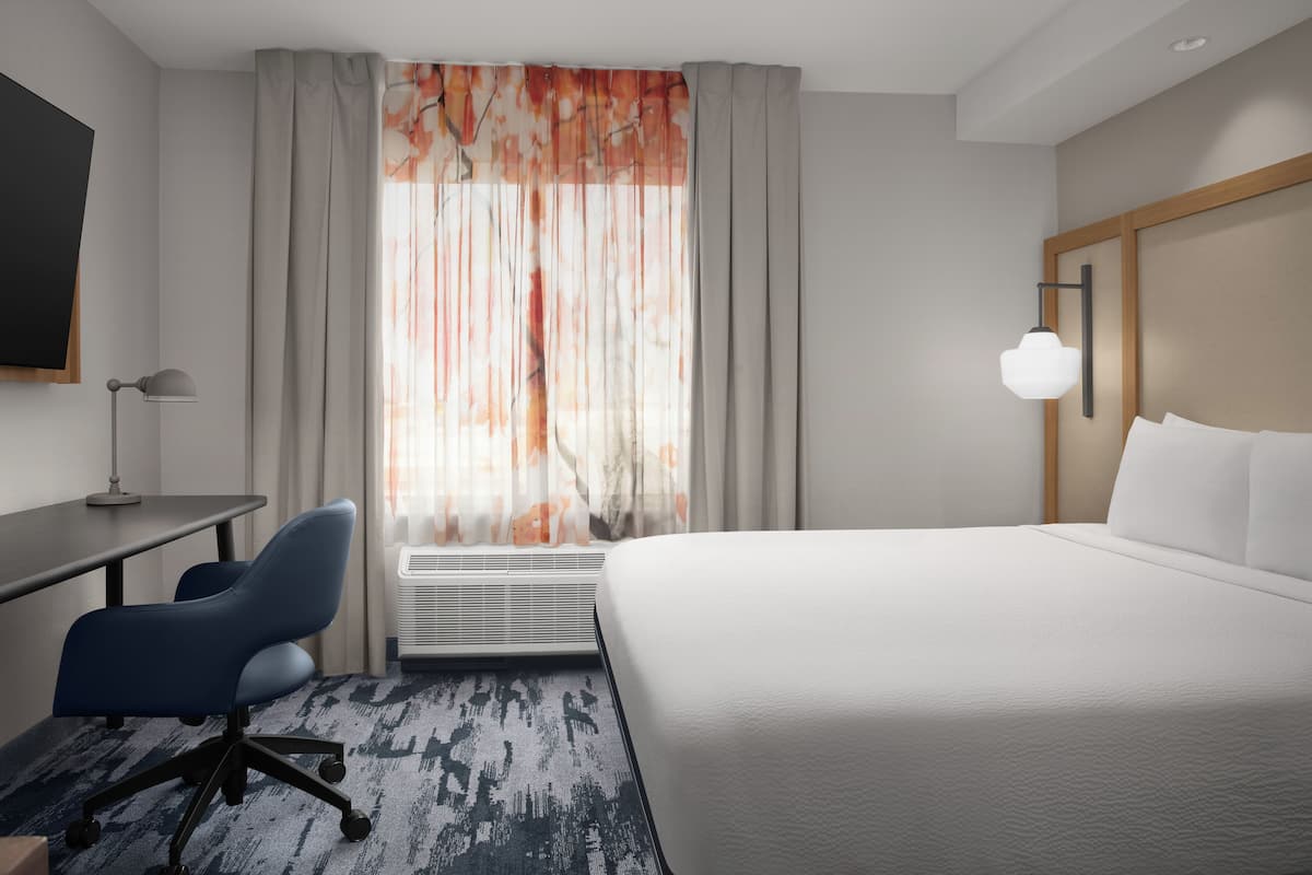 Hotellihuone, jossa on suuri sänky, työpöytä, tuoli ja ikkuna, jossa on verhot.