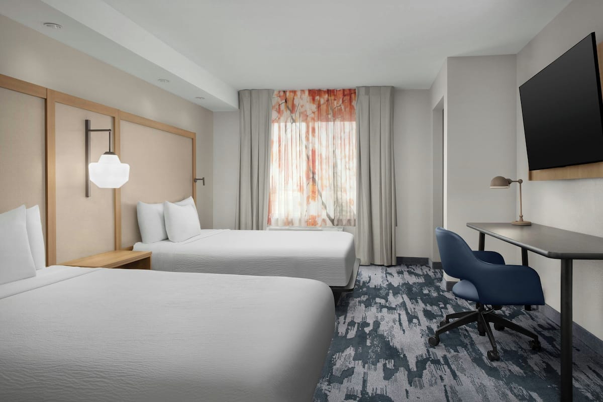 A hotel room with two beds, a desk, a chair, a TV, and a window with curtains.
