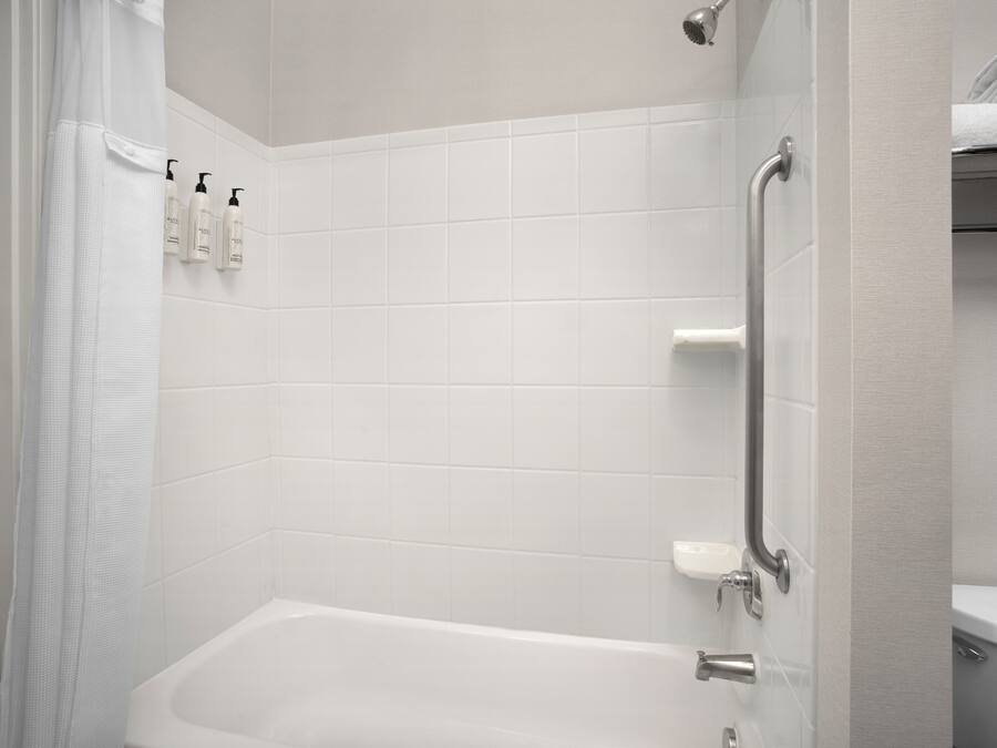 Ein Badezimmer mit einer weißen Badewanne, einer Duschkabine und einer Toilette. An der Wand befinden sich drei Flaschen Shampoo und Conditioner.