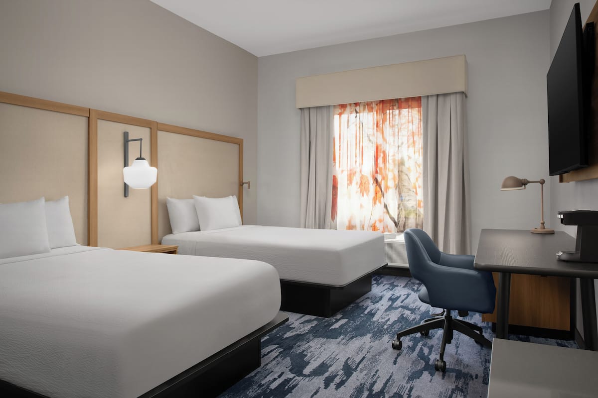 A hotel room with two beds, a desk, a chair, a TV, and a window with curtains.