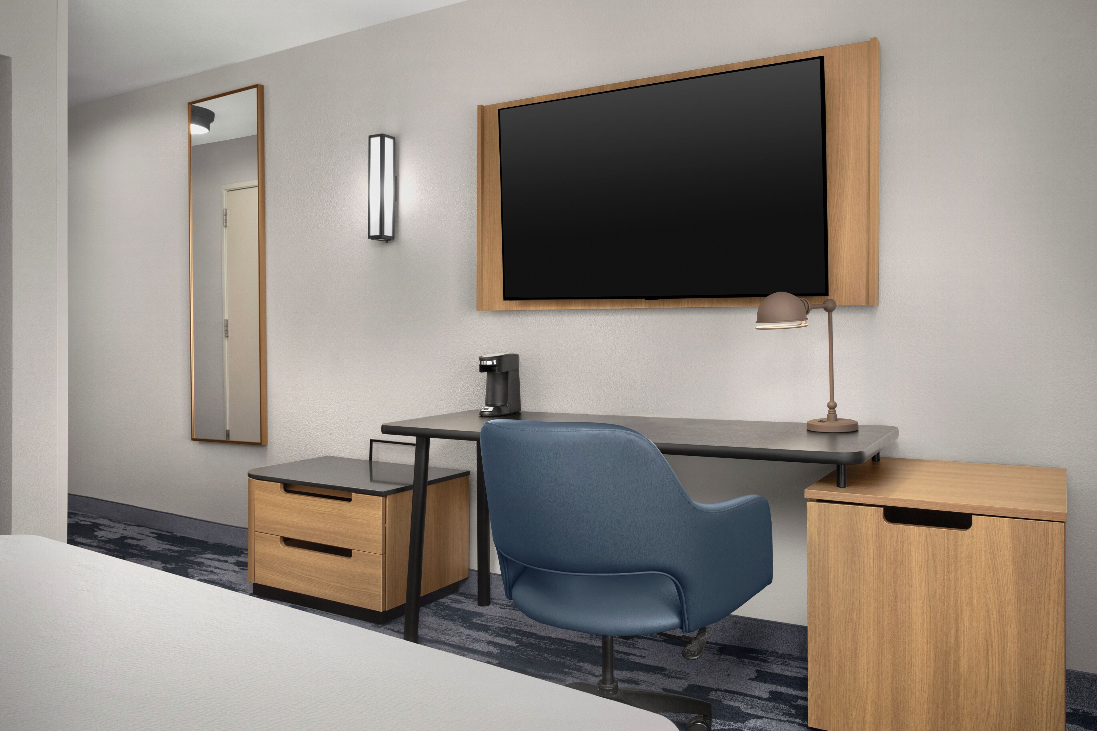 Een moderne hotelkamer met een bed, een bureau met stoel, een flatscreen televisie, een spiegel en een lamp.