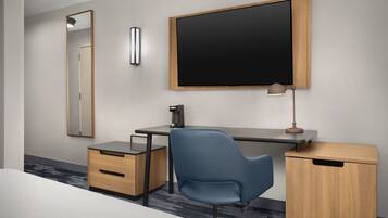 Een moderne hotelkamer met een bed, een bureau met stoel, een flatscreen televisie, een spiegel en een lamp.
