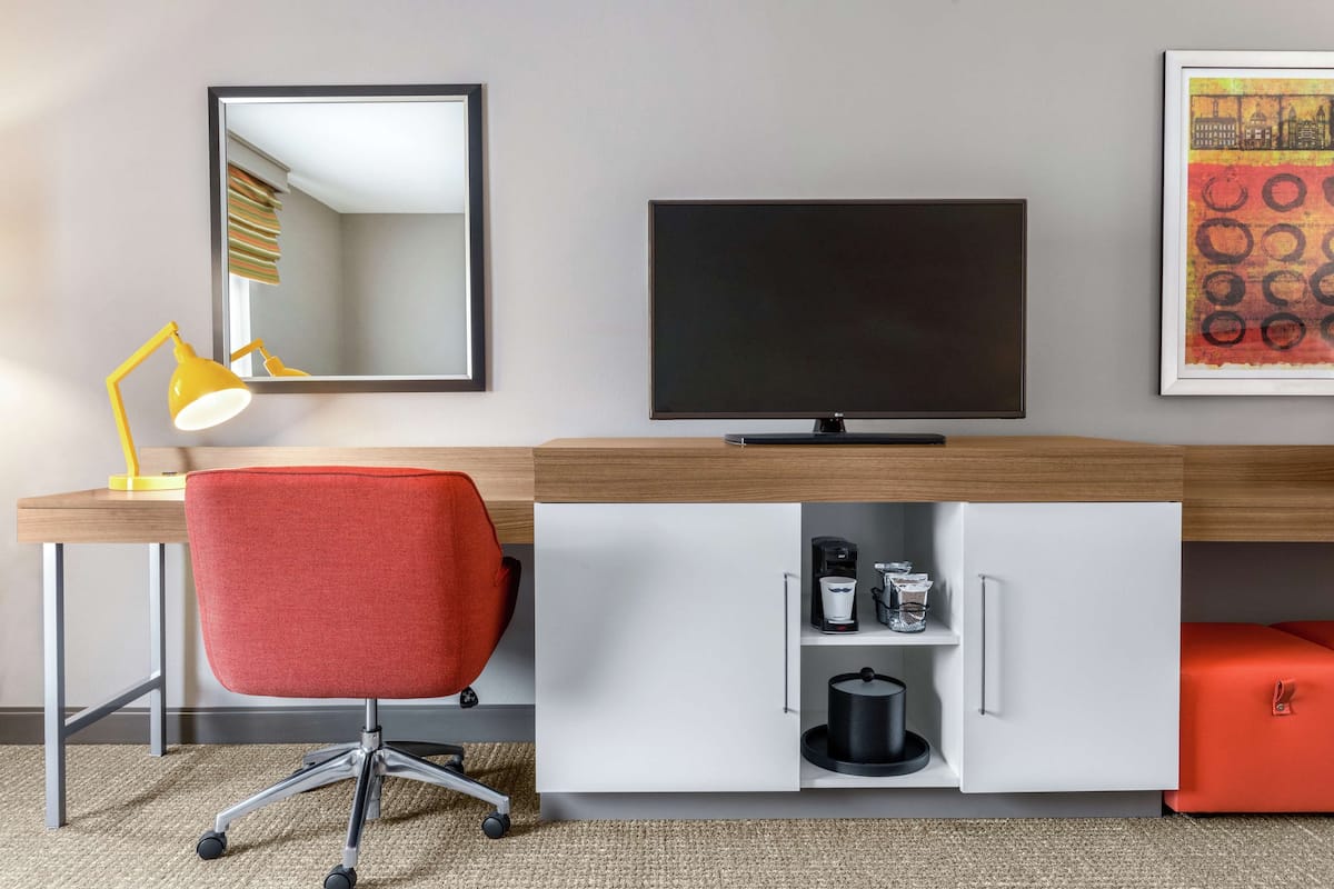 A modern office space with a desk, chair, TV, and storage unit.