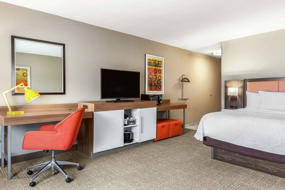 A hotel room with a bed, desk, chair, television, and storage units.