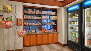 Una kitchenette con refrigerador, estantes llenos de refrigerios y bebidas, y un microondas.