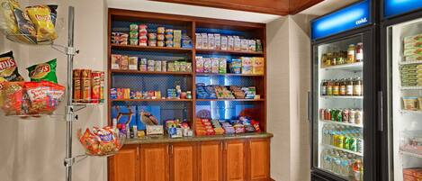 A kitchenette with a refrigerator, shelves stocked with snacks and beverages, and a microwave.