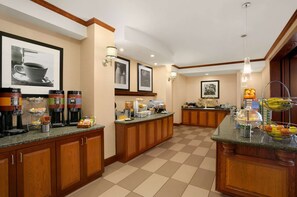 Zona de desayuno de hotel con un sistema de buffet, que incluye cafeteras, fruta y bollería.