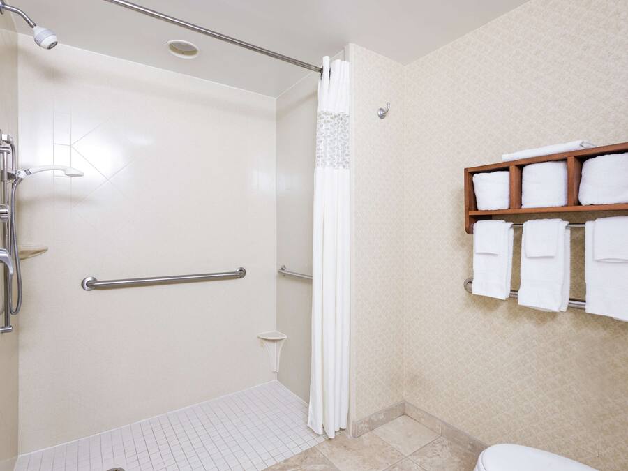Un baño con ducha, barras de apoyo, inodoro y perchero para toallas.