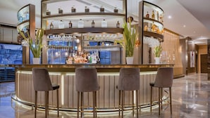 A bar area with a curved counter, multiple shelves with bottles and glasses, and three bar stools. - AC Hotel Firenze by Marriott (Florence)