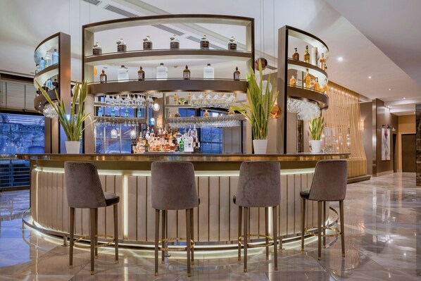 A bar area with a curved counter, multiple shelves with bottles and glasses, and three bar stools. - AC Hotel Firenze by Marriott (Florence)