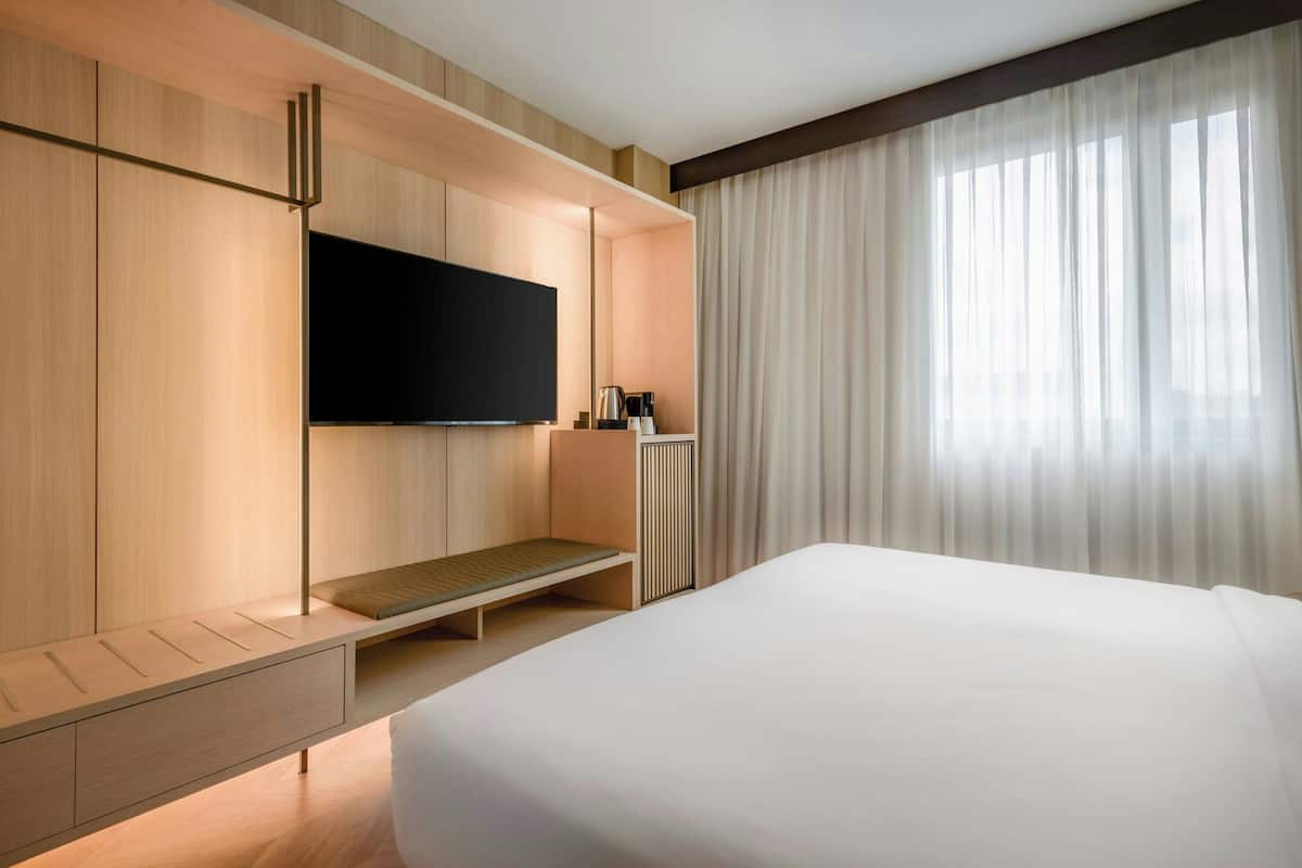 A modern hotel room with a large bed, built-in TV, and a seating area with a coffee machine.