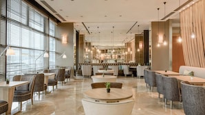 A modern hotel lobby with round tables, comfortable seating, and a central bar area. - AC Hotel Firenze by Marriott (Florence)