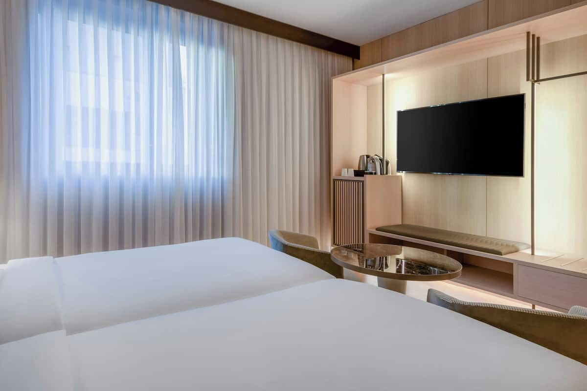 A hotel room with two beds, a TV, a small table, and a seating area.