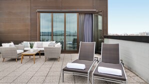 A rooftop terrace with wicker furniture, a glass door, and a view of the cityscape. - AC Hotel Firenze by Marriott (Florence)