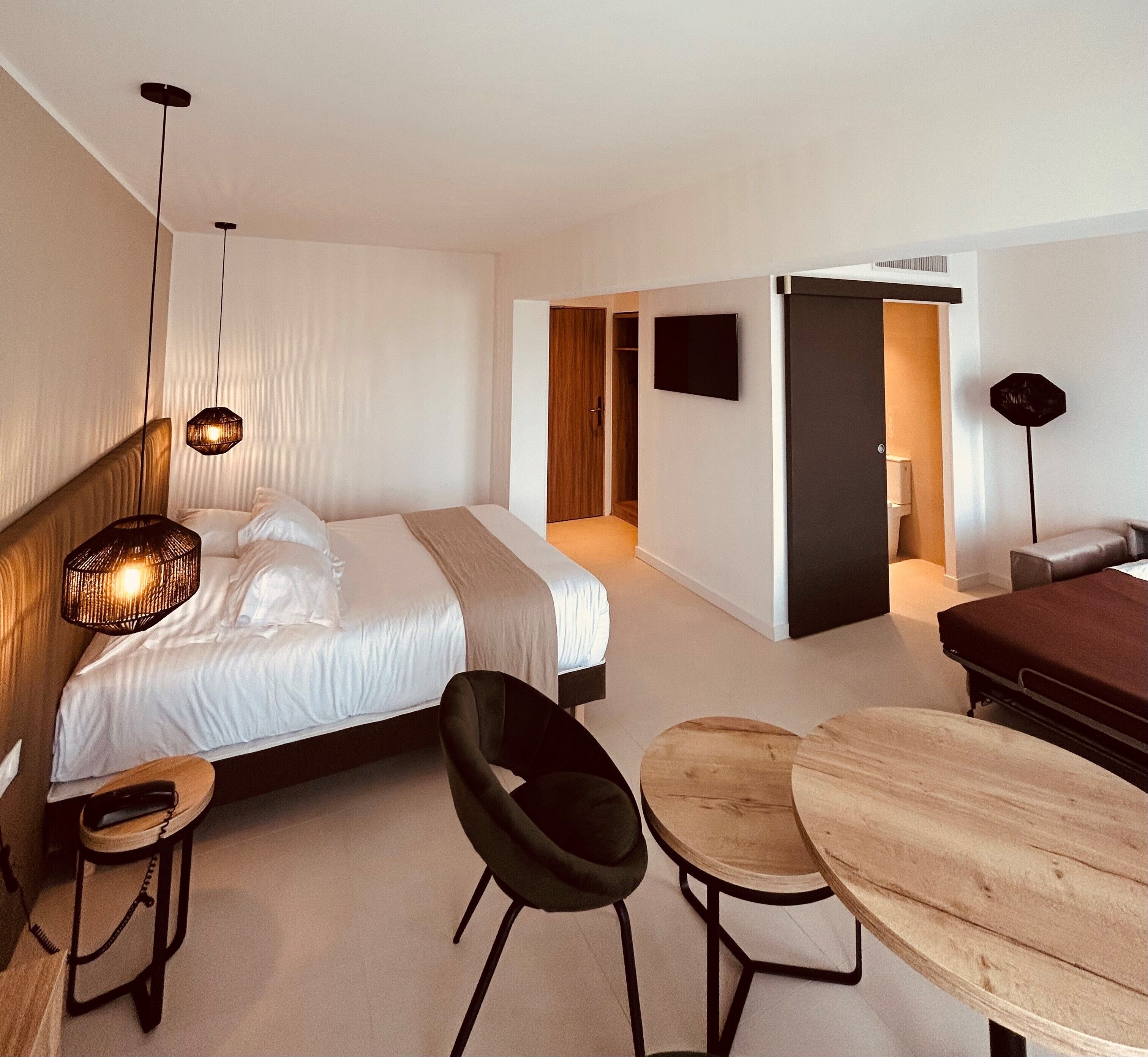 Een moderne hotelkamer met een bed, een bureau, een stoel, een klein tafeltje en een televisie.