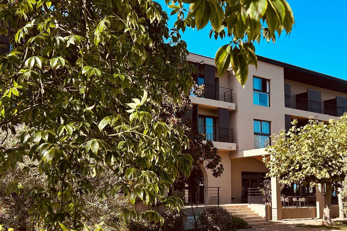 Un immeuble moderne à plusieurs étages, doté de balcons et entouré de verdure et d’arbres.