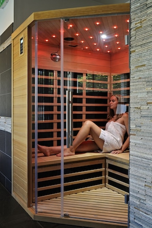 Een sauna met een glazen omheining, houten banken en een zichtbare stoomuitlaat.