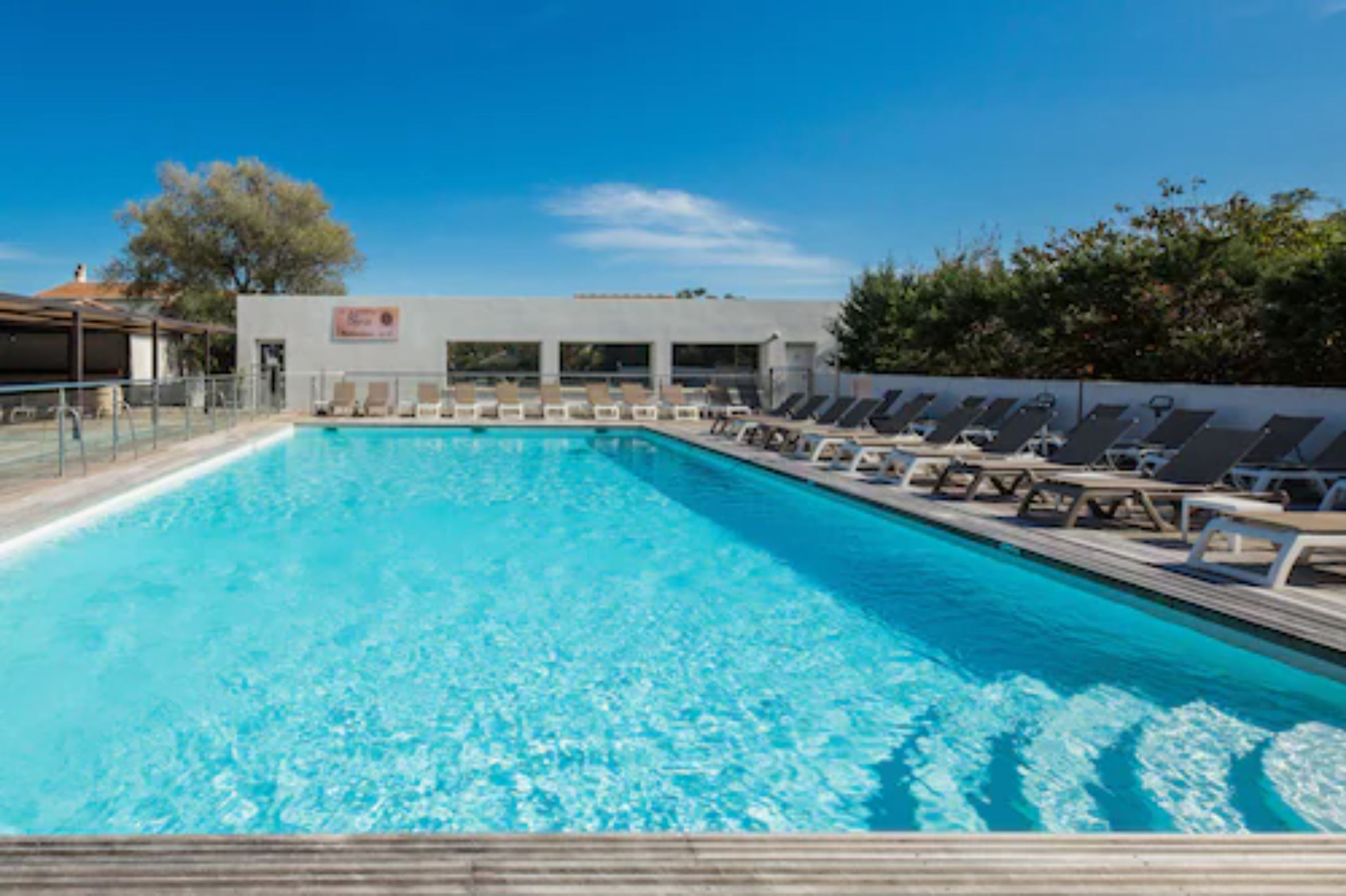 Una piscina rectangular con agua azul cristalina, rodeada de sillas de descanso y una terraza de madera.