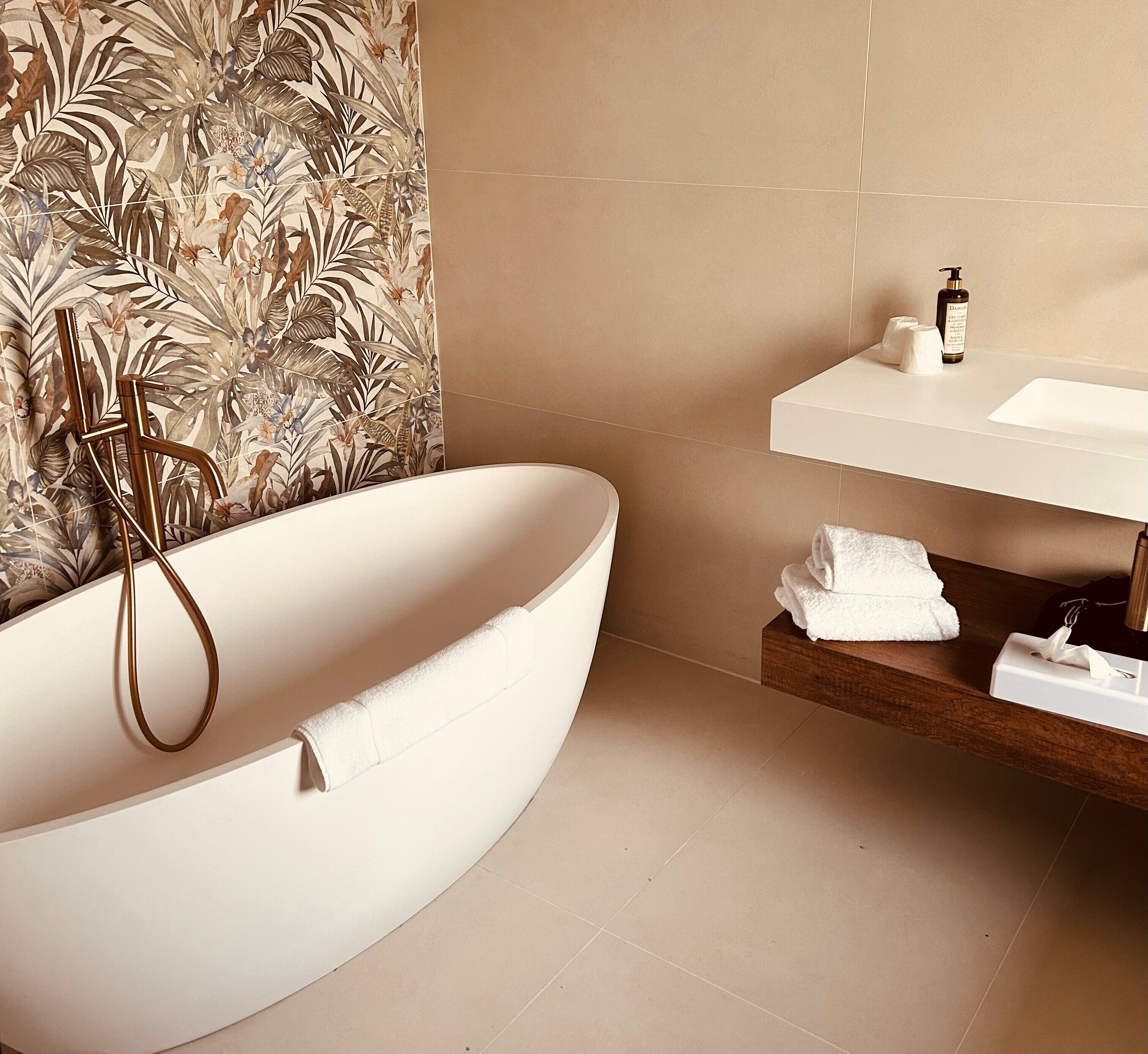 Ein modernes Badezimmer mit einer freistehenden Badewanne, einem Holzregal mit Handtüchern und einem wandmontierten Waschtisch mit einer Flasche und Seife.