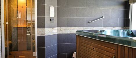 A bathroom with a glass shower enclosure, a wooden vanity with a green countertop, and a large bathtub.
