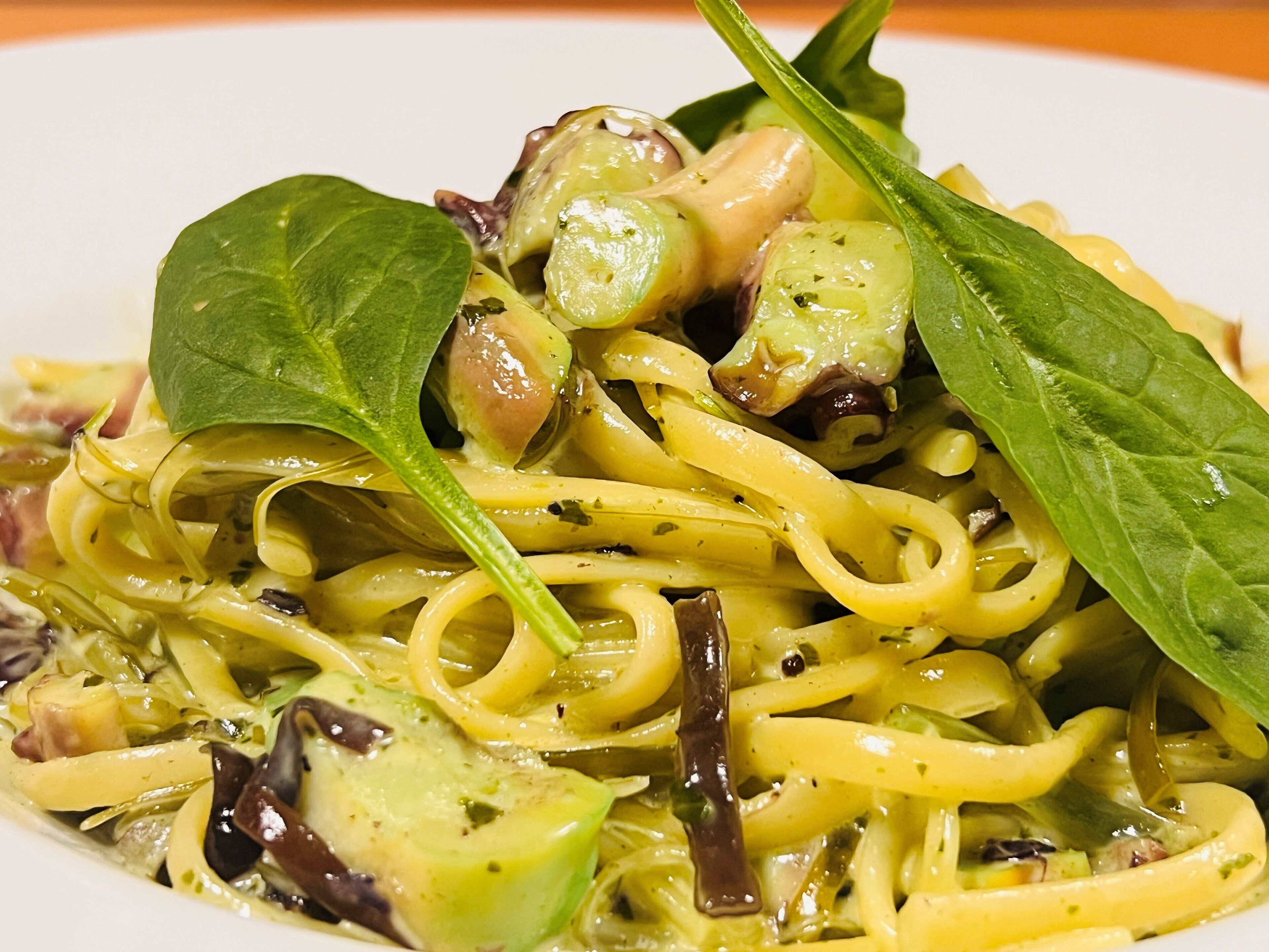 A plate of pasta with green leaves and mushrooms.