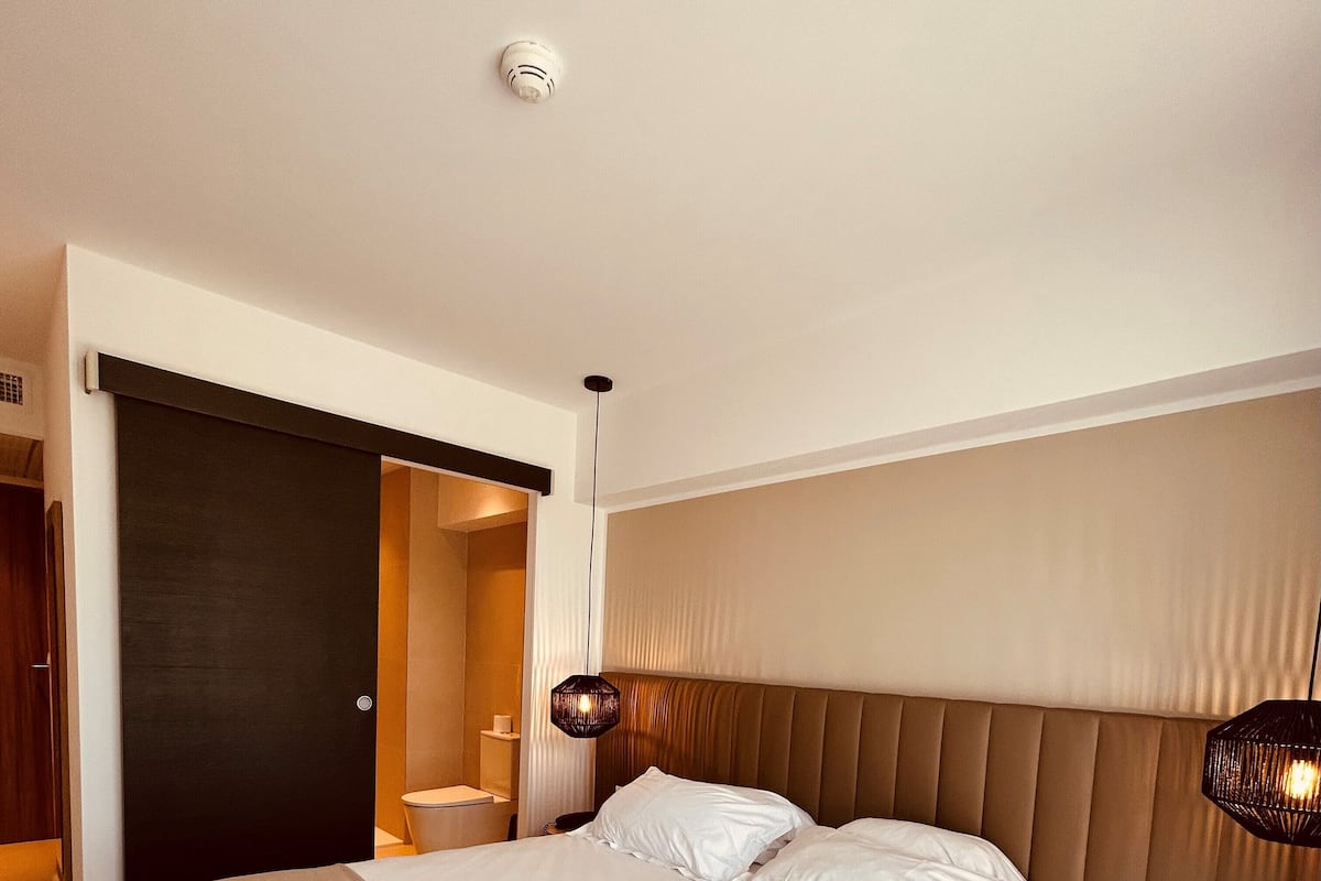 Une chambre d’hôtel moderne dotée d’un grand lit, d’une armoire intégrée, d’une table de chevet et d’une lampe suspendue.