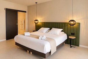 Una habitación de hotel moderna con una cama grande, dos mesitas de noche, una lámpara de pared y una puerta con un perchero.