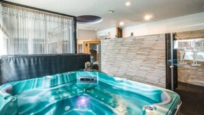Uma sala de spa moderna com uma banheira de hidromassagem ampla e transparente e um painel de parede de pedra.