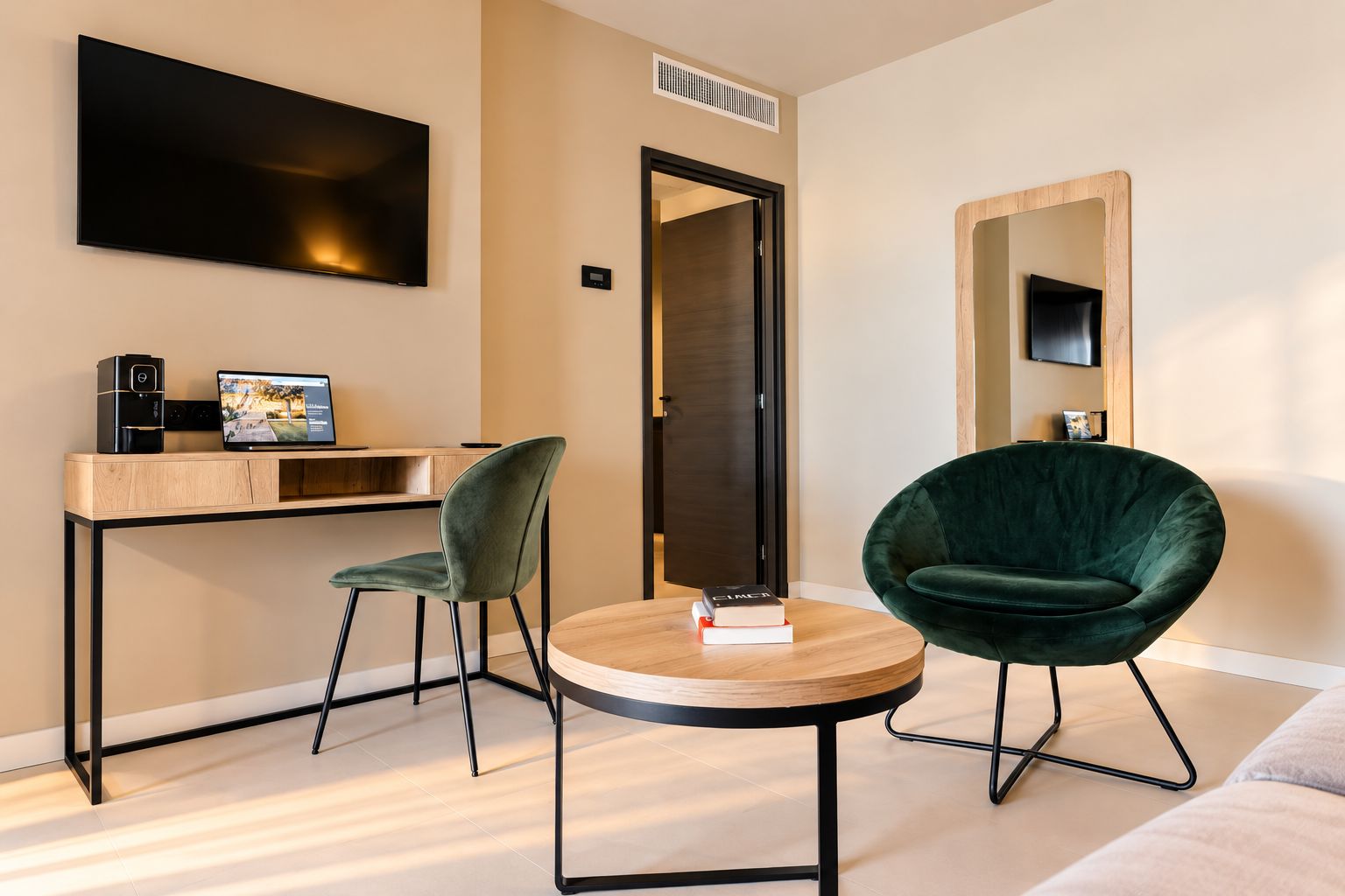 Ein modernes Zimmer mit einem Flachbildfernseher, einem Schreibtisch mit einem Laptop, einem grünen Stuhl, einem runden Tisch mit Büchern und einem Spiegel.