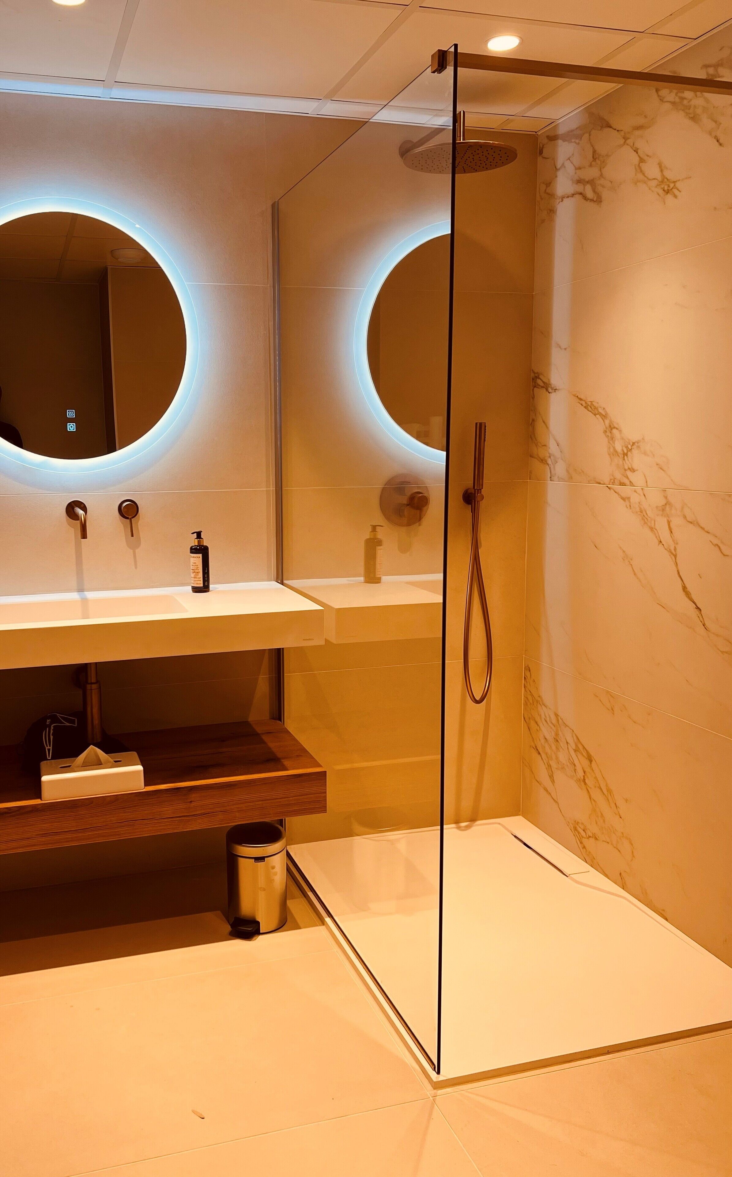 A modern bathroom with two sinks, a glass shower enclosure, and marble walls.